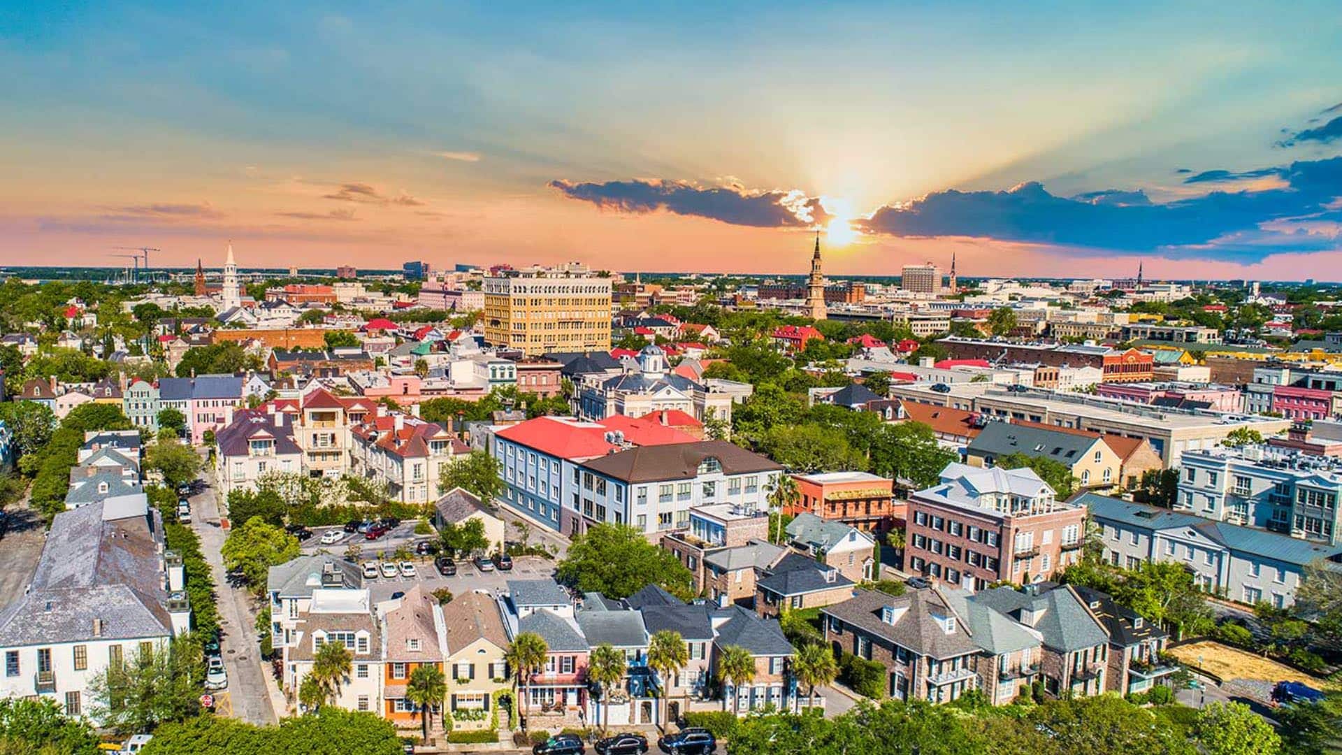Aerial view of residential and downtown buildings surrounded by green trees with the sun in the background